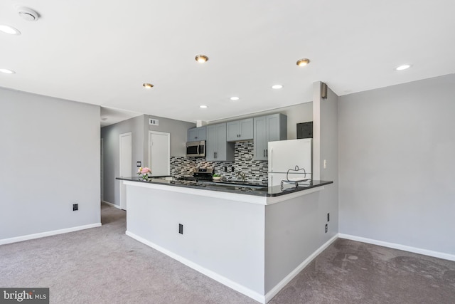 kitchen with backsplash, dark countertops, stainless steel appliances, carpet floors, and baseboards