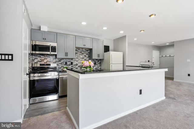 kitchen featuring carpet, a kitchen island, appliances with stainless steel finishes, dark countertops, and tasteful backsplash