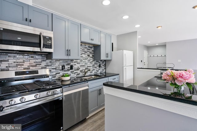 kitchen featuring dark countertops, tasteful backsplash, appliances with stainless steel finishes, wood finished floors, and a sink