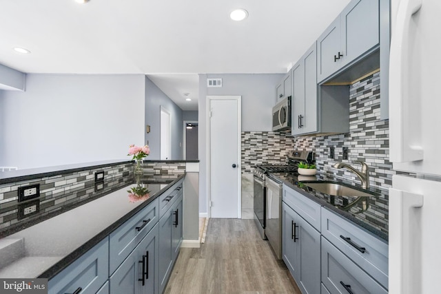 kitchen featuring dark stone countertops, visible vents, light wood-style flooring, a sink, and stainless steel appliances