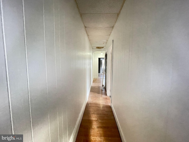 corridor with a paneled ceiling, baseboards, and dark wood-style flooring