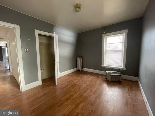 unfurnished bedroom featuring a closet, radiator heating unit, wood finished floors, and baseboards