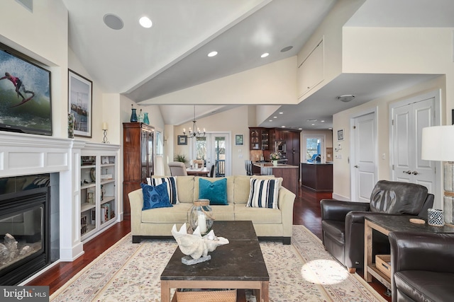 living area featuring a tile fireplace, dark wood-type flooring, lofted ceiling, and an inviting chandelier