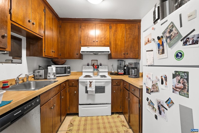 kitchen featuring brown cabinets, light countertops, appliances with stainless steel finishes, a sink, and under cabinet range hood