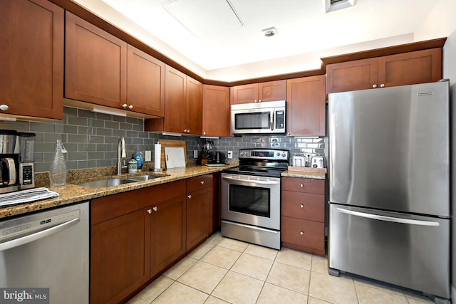 kitchen with a sink, backsplash, stainless steel appliances, light tile patterned flooring, and light stone countertops