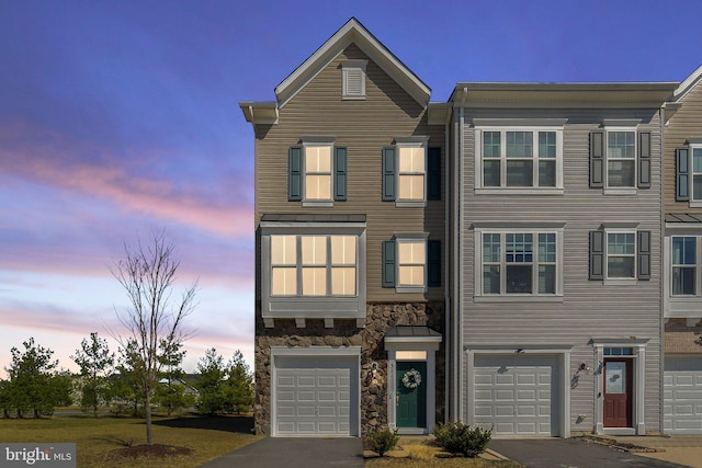 townhome / multi-family property with aphalt driveway, stone siding, and a garage