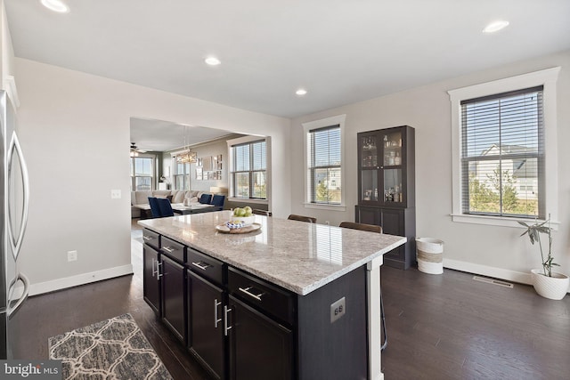 kitchen with dark wood-type flooring, light stone countertops, baseboards, and a kitchen island