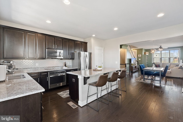 kitchen with a sink, stainless steel appliances, dark brown cabinetry, open floor plan, and a center island