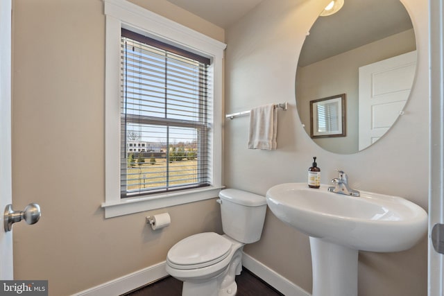 half bathroom featuring toilet, wood finished floors, baseboards, and a sink