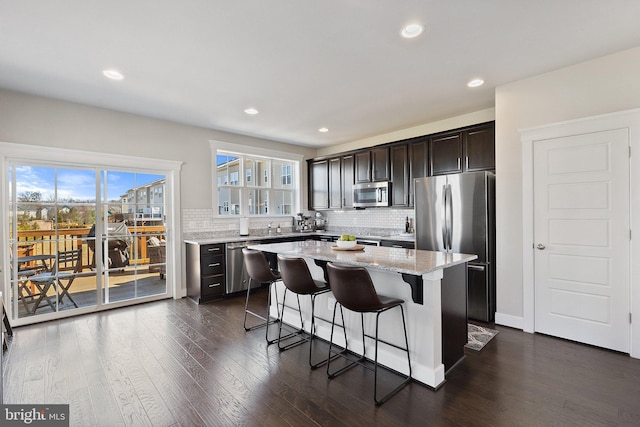 kitchen featuring light stone counters, dark wood-style floors, appliances with stainless steel finishes, a kitchen breakfast bar, and a center island