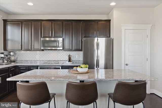 kitchen with dark brown cabinetry, decorative backsplash, appliances with stainless steel finishes, and a breakfast bar area