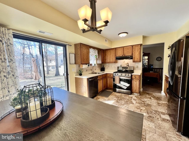 kitchen featuring stainless steel gas stove, freestanding refrigerator, a sink, dishwasher, and brown cabinets