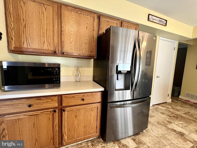 kitchen with visible vents, brown cabinets, stone finish floor, appliances with stainless steel finishes, and light countertops