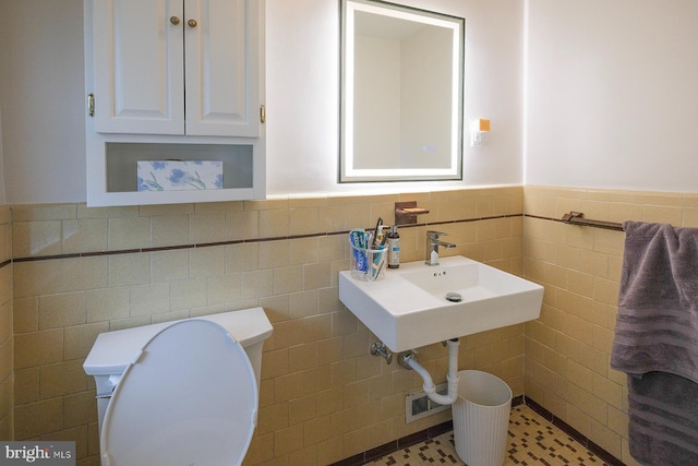 half bathroom featuring a wainscoted wall, toilet, and tile walls