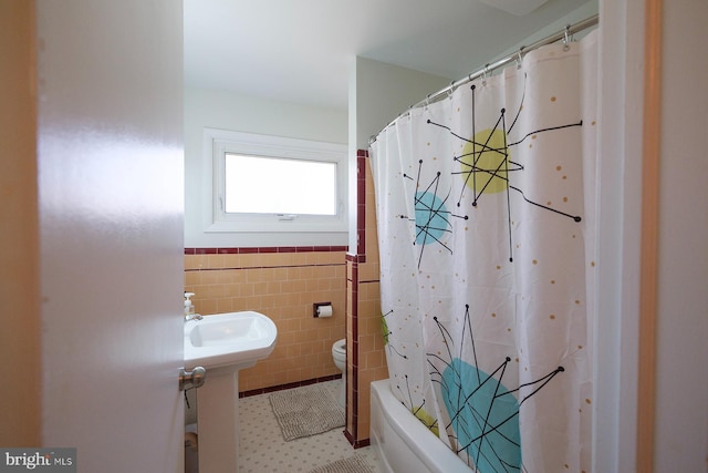 bathroom with a wainscoted wall, shower / bath combo with shower curtain, toilet, and tile walls