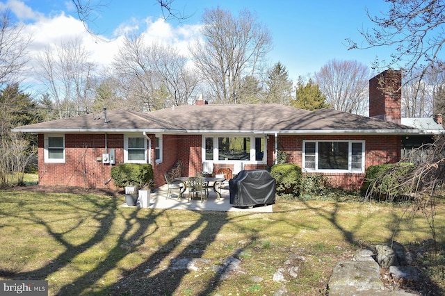 rear view of property featuring brick siding, a yard, a chimney, and a patio