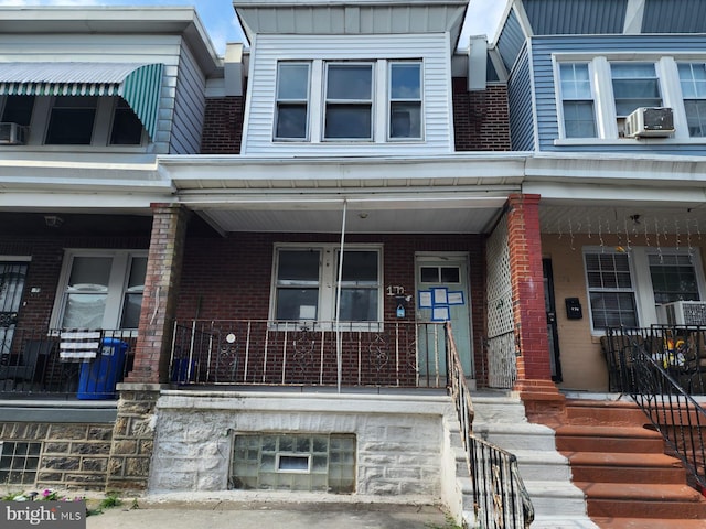 view of property featuring a porch, cooling unit, brick siding, and board and batten siding