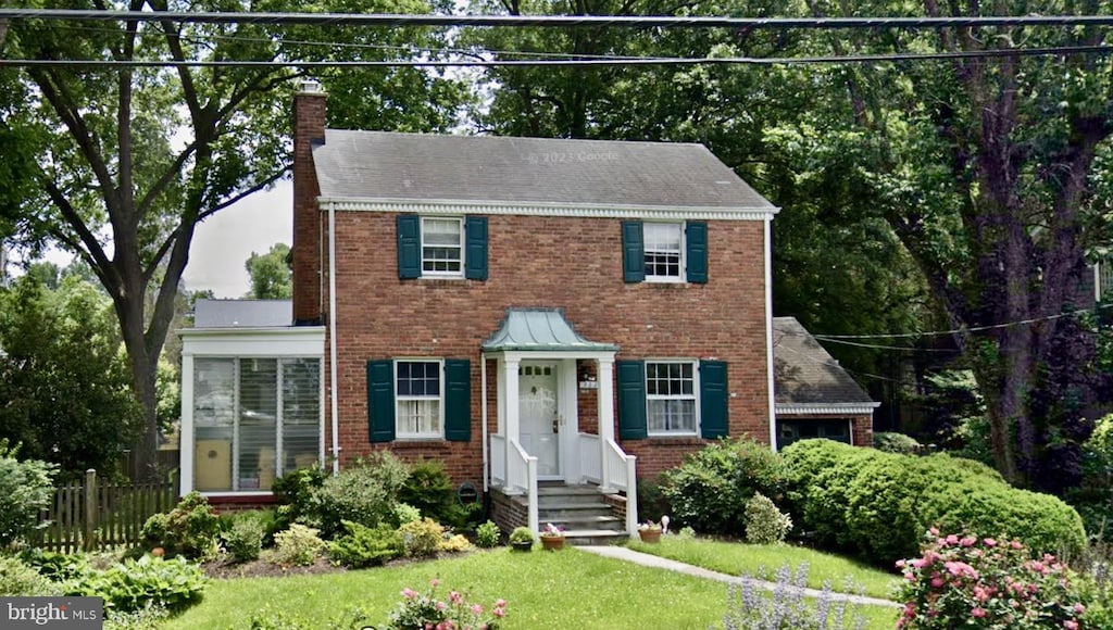 colonial inspired home with a front yard, a chimney, fence, and brick siding