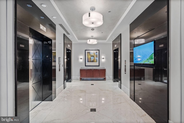 hallway with a tray ceiling, marble finish floor, and baseboards