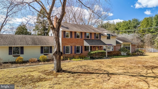 view of front facade with brick siding, roof with shingles, a chimney, and fence