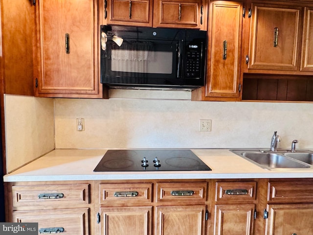 kitchen with a sink, black appliances, brown cabinetry, and light countertops