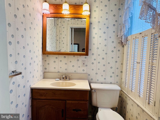 bathroom with toilet, wallpapered walls, and vanity