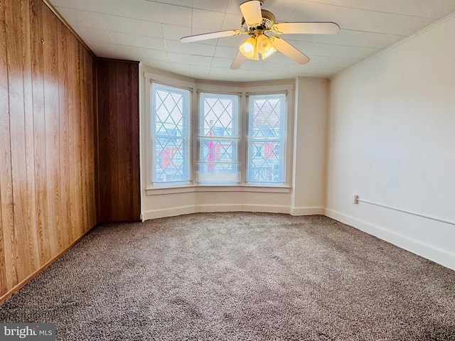 unfurnished room featuring wooden walls, crown molding, baseboards, ceiling fan, and carpet floors