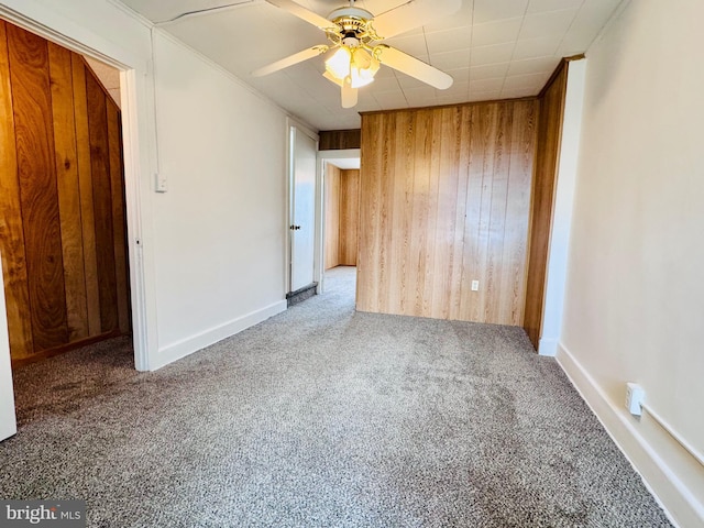 empty room with wood walls, a ceiling fan, and carpet floors