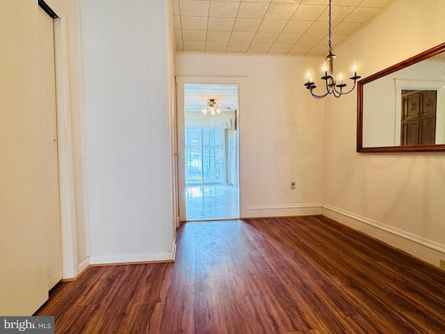 empty room with a notable chandelier, baseboards, and wood finished floors