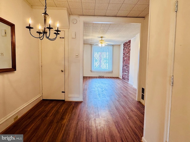 unfurnished dining area with ceiling fan with notable chandelier, dark wood-style floors, and baseboards