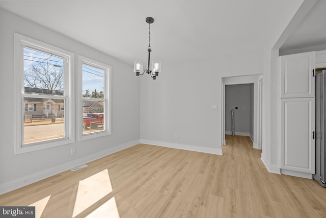 unfurnished dining area featuring baseboards, light wood finished floors, visible vents, and a notable chandelier