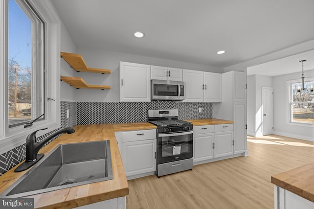 kitchen featuring butcher block countertops, appliances with stainless steel finishes, white cabinetry, open shelves, and a sink