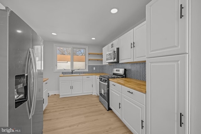 kitchen with butcher block countertops, a sink, white cabinets, appliances with stainless steel finishes, and light wood-type flooring