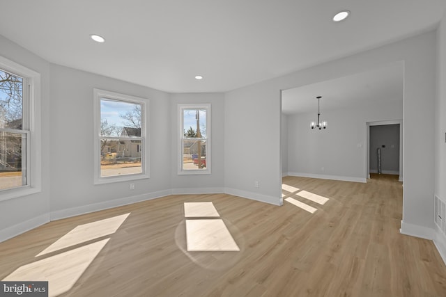 unfurnished living room featuring baseboards, recessed lighting, light wood-type flooring, and an inviting chandelier