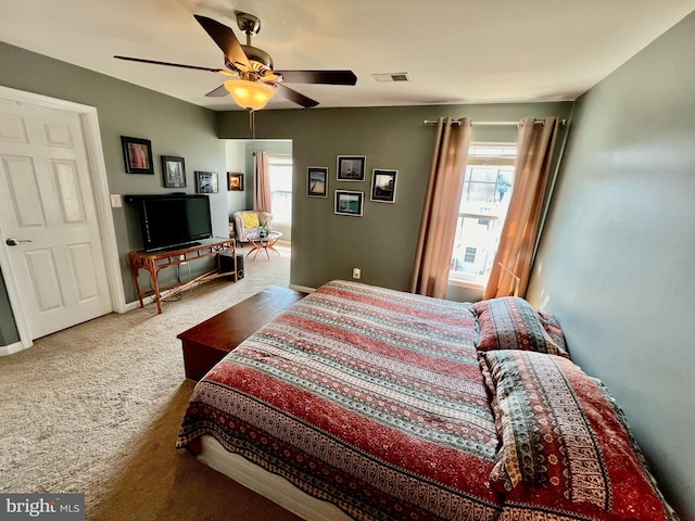 carpeted bedroom featuring visible vents, multiple windows, baseboards, and a ceiling fan