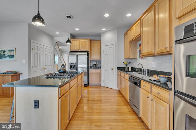 kitchen featuring a kitchen island, light wood-style flooring, a sink, decorative backsplash, and appliances with stainless steel finishes