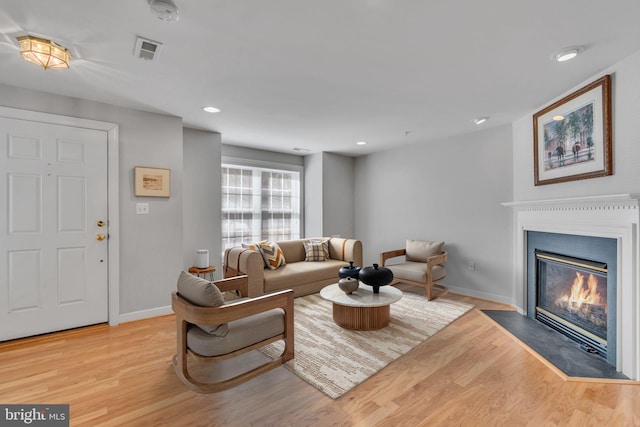 living room with visible vents, a fireplace with flush hearth, baseboards, and light wood-style flooring