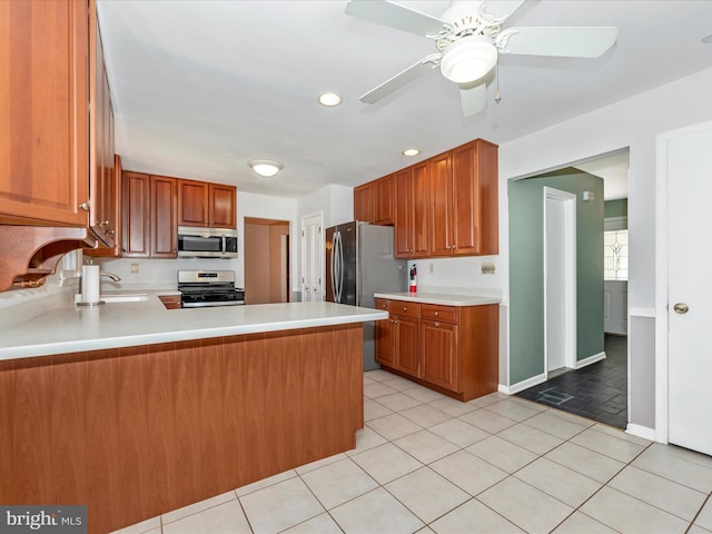 kitchen featuring a peninsula, light tile patterned flooring, a sink, stainless steel appliances, and light countertops