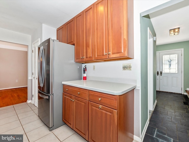 kitchen with brown cabinetry, light countertops, freestanding refrigerator, and baseboards