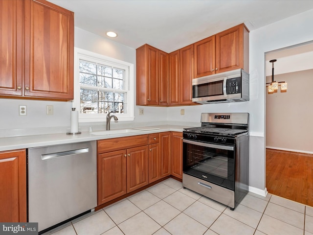 kitchen with light tile patterned floors, brown cabinetry, a sink, stainless steel appliances, and light countertops