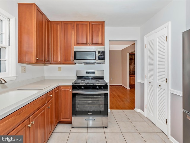 kitchen with brown cabinetry, light countertops, light tile patterned flooring, stainless steel appliances, and a sink