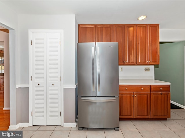 kitchen featuring light tile patterned floors, brown cabinetry, light countertops, and freestanding refrigerator