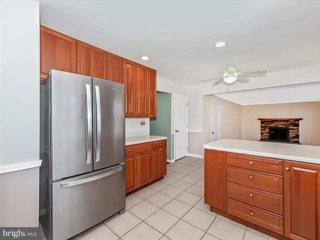 kitchen featuring light countertops, freestanding refrigerator, light tile patterned flooring, brown cabinetry, and a ceiling fan