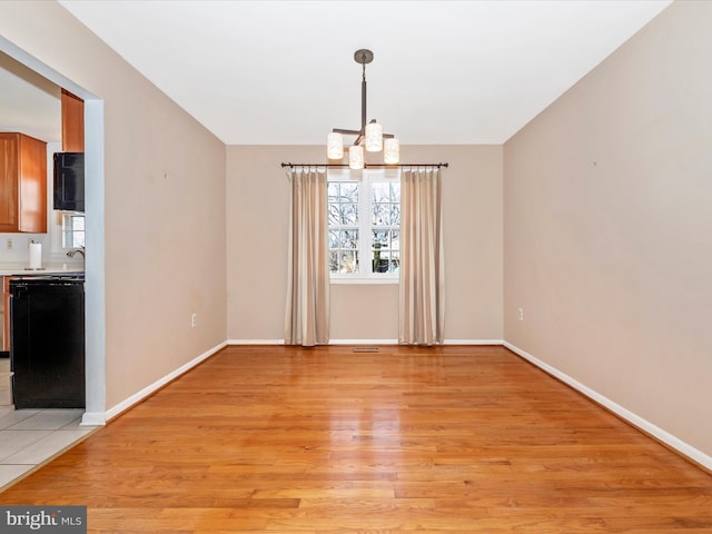 unfurnished dining area with a notable chandelier, baseboards, and light wood-style floors