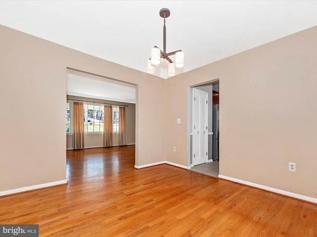 unfurnished room with light wood-style flooring, a notable chandelier, and baseboards