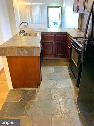 kitchen with a peninsula, black appliances, stone tile floors, and a sink