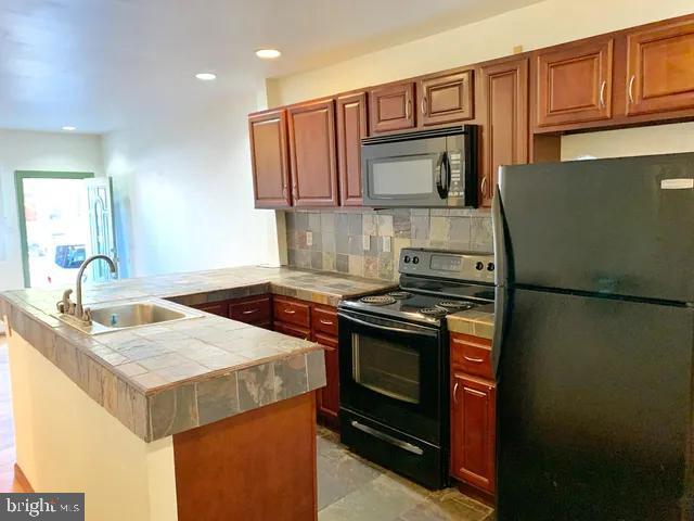 kitchen with backsplash, a sink, tile countertops, and black appliances