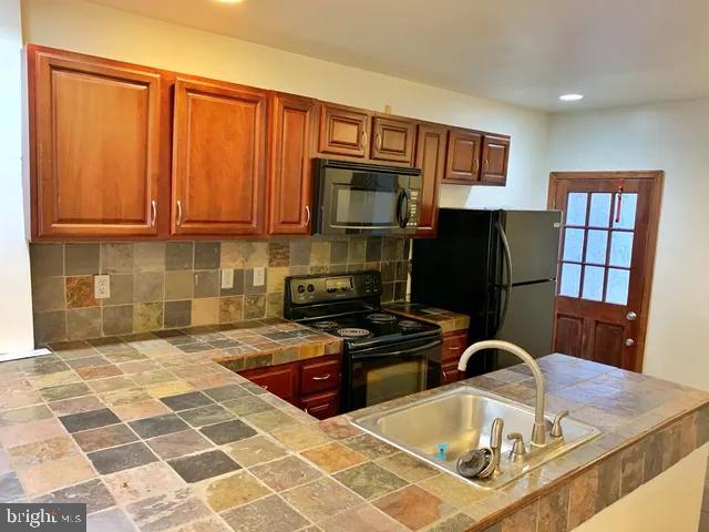 kitchen with tile countertops, brown cabinets, a sink, black appliances, and backsplash