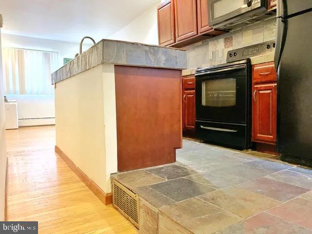 kitchen featuring a baseboard heating unit, baseboards, decorative backsplash, black appliances, and light wood finished floors