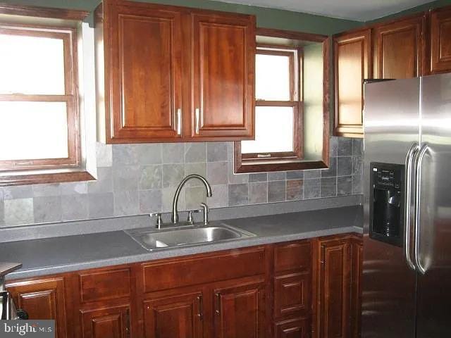 kitchen featuring backsplash, brown cabinets, a sink, and stainless steel refrigerator with ice dispenser